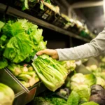 Shopper selecting fresh leafy greens in a grocery produce aisle reflecting food safety standards.