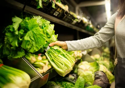 Shopper selecting fresh leafy greens in a grocery produce aisle reflecting food safety standards.