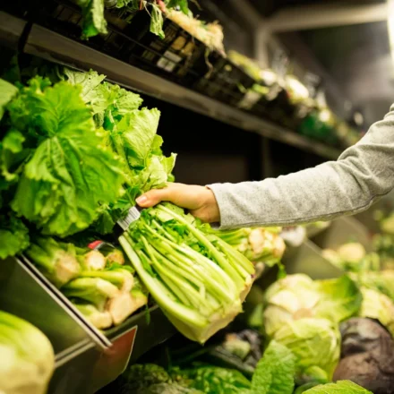 Shopper selecting fresh leafy greens in a grocery produce aisle reflecting food safety standards.