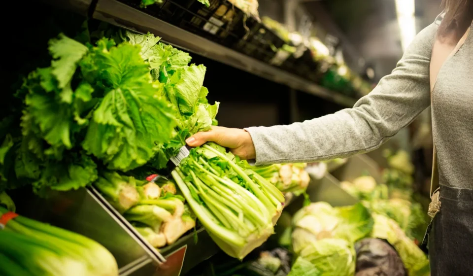 Shopper selecting fresh leafy greens in a grocery produce aisle reflecting food safety standards.