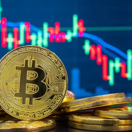 Golden Bitcoin coins stacked in front of a blue candlestick trading chart showing price movement