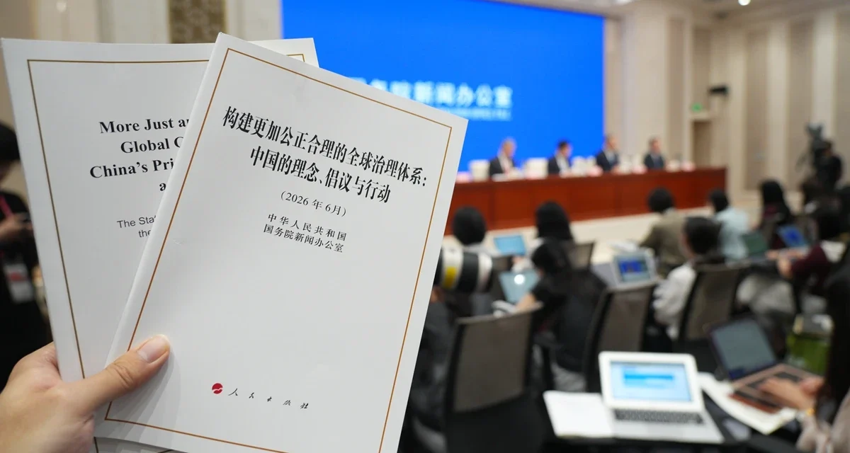 Hand holding China's global governance white paper during an international press briefing in Beijing.