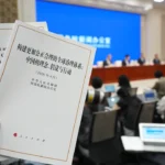 Hand holding China's global governance white paper during an international press briefing in Beijing.