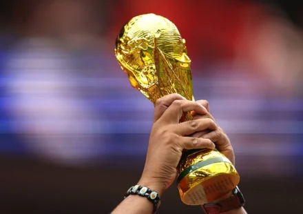 Hands raise the FIFA World Cup trophy before a blurred stadium crowd during an international football event.
