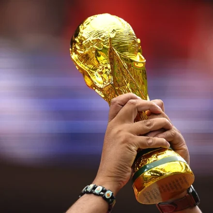 Hands raise the FIFA World Cup trophy before a blurred stadium crowd during an international football event.
