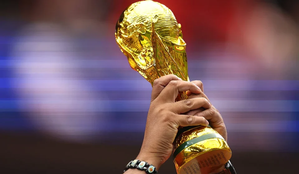 Hands raise the FIFA World Cup trophy before a blurred stadium crowd during an international football event.