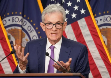 Federal Reserve Chair speaks after holding interest rates steady with US flags displayed behind podium.
