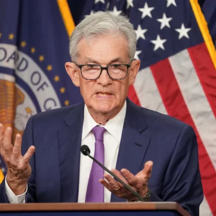 Federal Reserve Chair speaks after holding interest rates steady with US flags displayed behind podium.