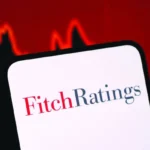 Fitch Ratings logo displayed on a smartphone with a falling market graph highlighting credit risk concerns.