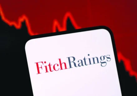 Fitch Ratings logo displayed on a smartphone with a falling market graph highlighting credit risk concerns.