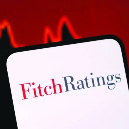 Fitch Ratings logo displayed on a smartphone with a falling market graph highlighting credit risk concerns.