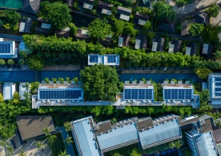 Aerial view of eco friendly residential buildings with rooftop solar panels surrounded by lush greenery.