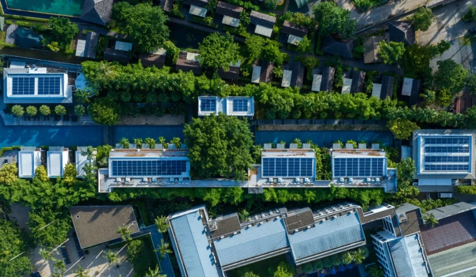 Aerial view of eco friendly residential buildings with rooftop solar panels surrounded by lush greenery.