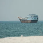 A traditional blue and white wooden dhow boat floating on calm blue ocean waters near a shoreline.