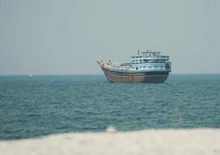 A traditional blue and white wooden dhow boat floating on calm blue ocean waters near a shoreline.