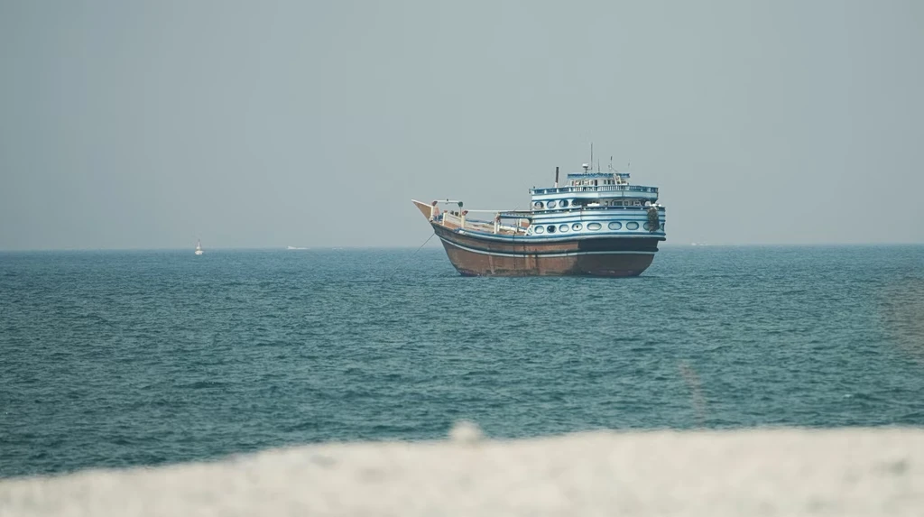 A traditional blue and white wooden dhow boat floating on calm blue ocean waters near a shoreline.
