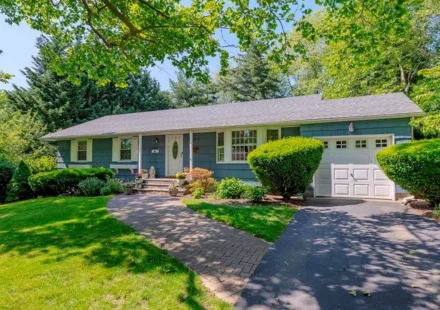 Blue single family home with attached garage, landscaped front yard, curved walkway, and mature trees.
