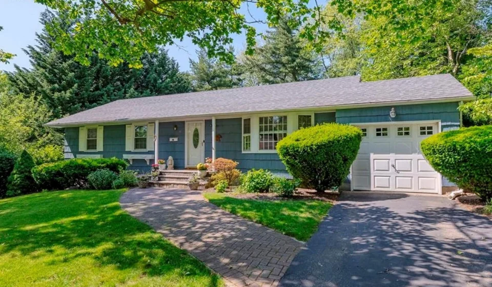 Blue single family home with attached garage, landscaped front yard, curved walkway, and mature trees.
