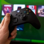 Black gaming controller held before a cloud gaming interface on a screen showing next generation console services.