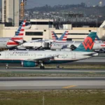 American Airlines and another commercial jet taxi on an airport runway amid busy terminal operations and traffic.