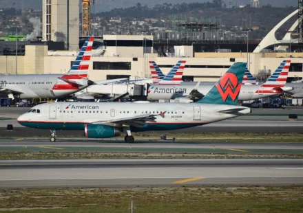 American Airlines and another commercial jet taxi on an airport runway amid busy terminal operations and traffic.