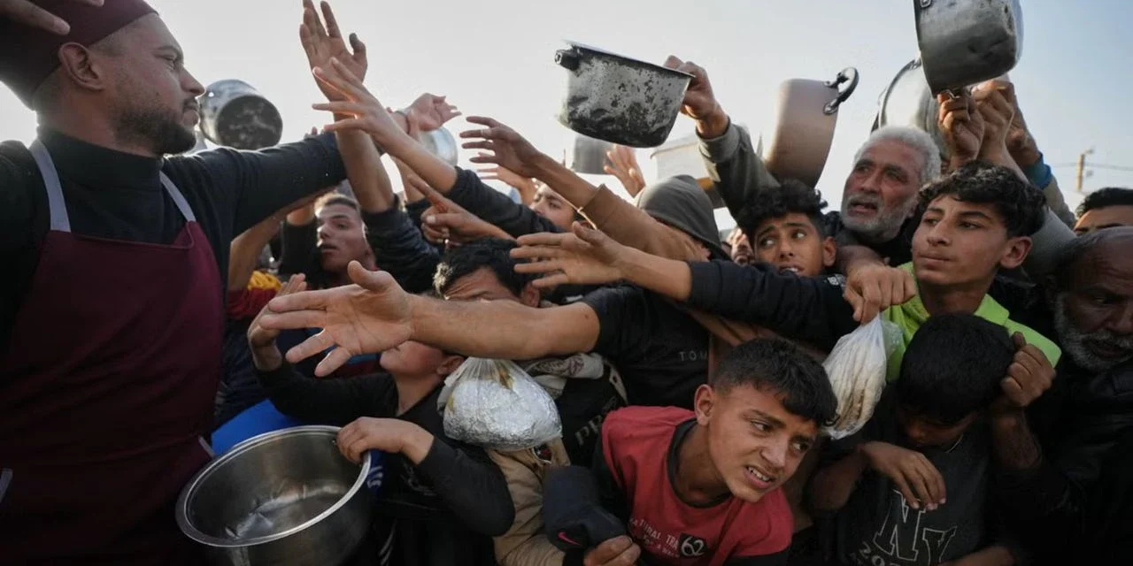Crowd reaches for food as a volunteer distributes meals to families during a humanitarian aid distribution.