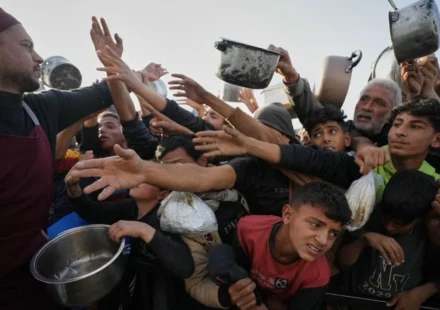 Crowd reaches for food as a volunteer distributes meals to families during a humanitarian aid distribution.