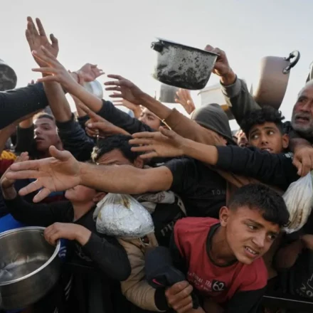 Crowd reaches for food as a volunteer distributes meals to families during a humanitarian aid distribution.
