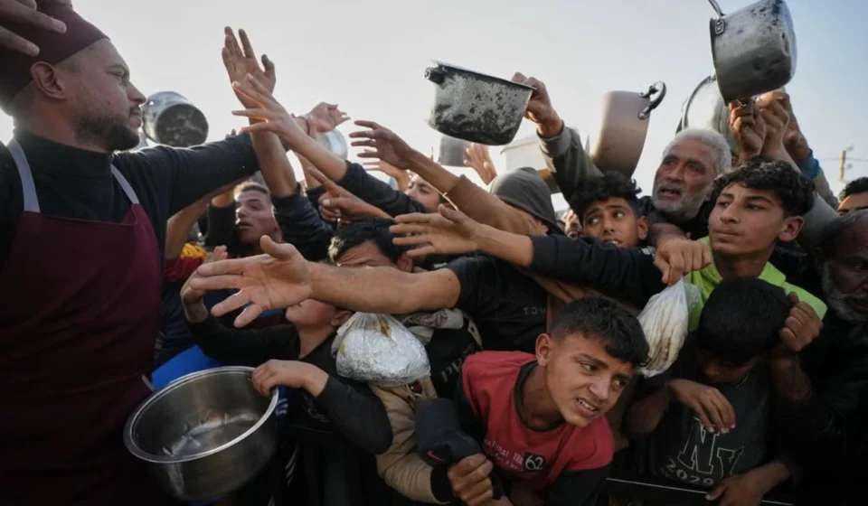 Crowd reaches for food as a volunteer distributes meals to families during a humanitarian aid distribution.