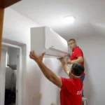 Technicians install a wall mounted smart air conditioner in a home to improve energy efficient cooling during heatwaves.