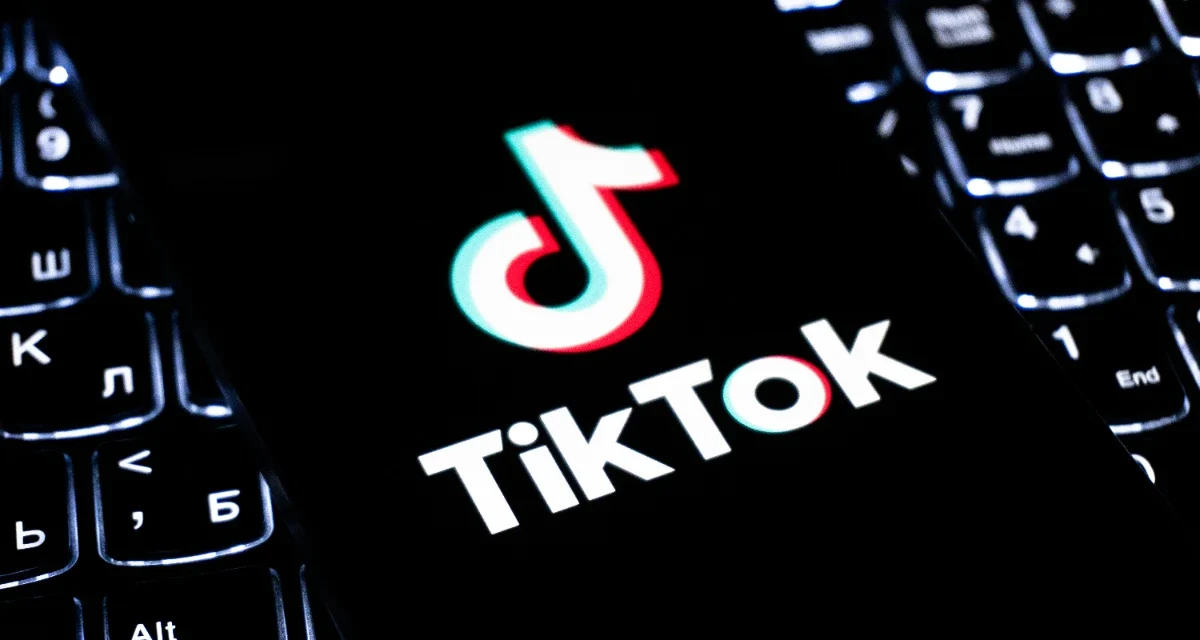 TikTok logo displayed on a smartphone over a keyboard, illustrating updated live shopping policies.!