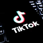 TikTok logo displayed on a smartphone over a keyboard, illustrating updated live shopping policies.!