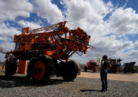 Large agricultural sprayer on display as a visitor examines modern farm equipment under a cloudy sky.