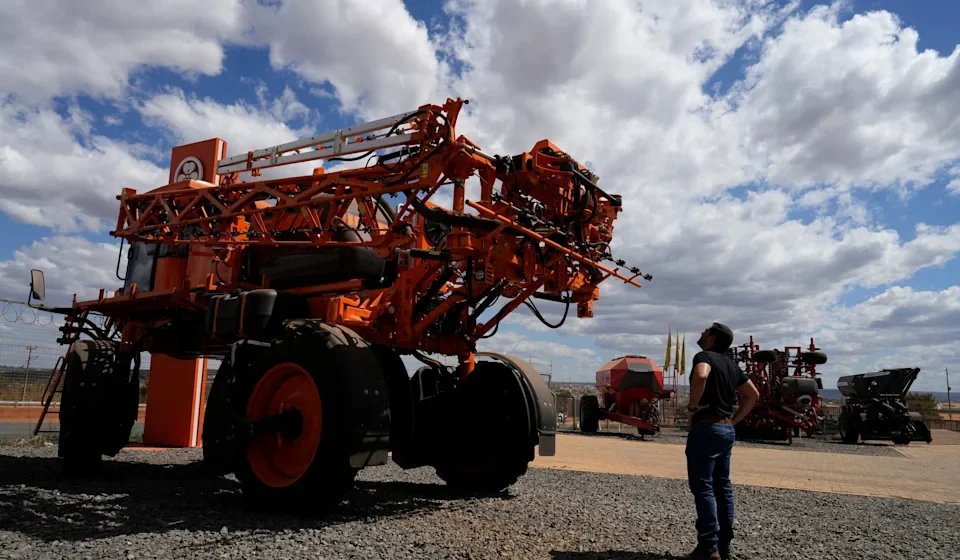 Large agricultural sprayer on display as a visitor examines modern farm equipment under a cloudy sky.