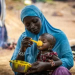 Mother feeding child with nutritional meal highlights hunger relief efforts amid global food crisis.