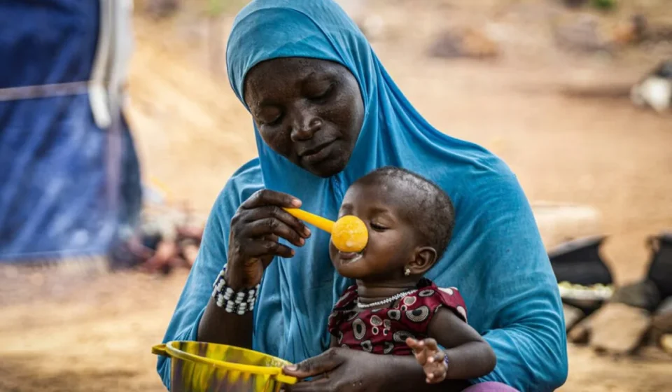 Mother feeding child with nutritional meal highlights hunger relief efforts amid global food crisis.