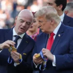 FIFA President and Donald Trump examine World Cup medals during a public event before a crowd outdoors.