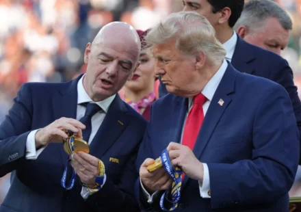 FIFA President and Donald Trump examine World Cup medals during a public event before a crowd outdoors.