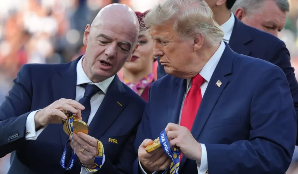 FIFA President and Donald Trump examine World Cup medals during a public event before a crowd outdoors.