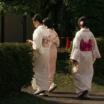 Japanese women wearing traditional kimonos walk through a peaceful park, reflecting cultural heritage.