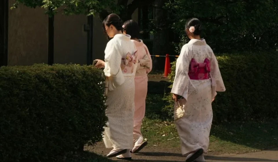 Japanese women wearing traditional kimonos walk through a peaceful park, reflecting cultural heritage.