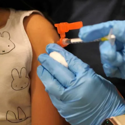 Healthcare worker prepares to vaccinate a child, highlighting updated immunization and public health efforts.