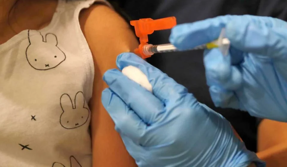 Healthcare worker prepares to vaccinate a child, highlighting updated immunization and public health efforts.