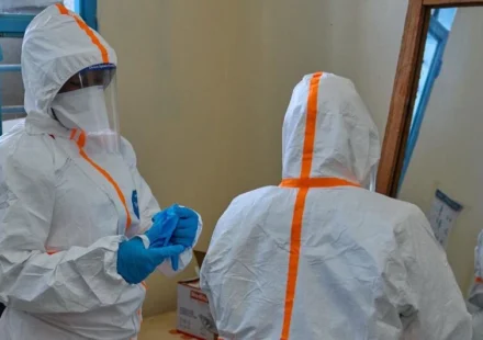 Healthcare workers wearing full protective suits prepare for Ebola response inside a medical facility room.