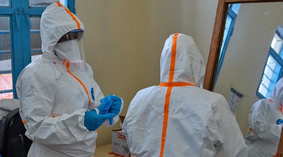 Healthcare workers wearing full protective suits prepare for Ebola response inside a medical facility room.
