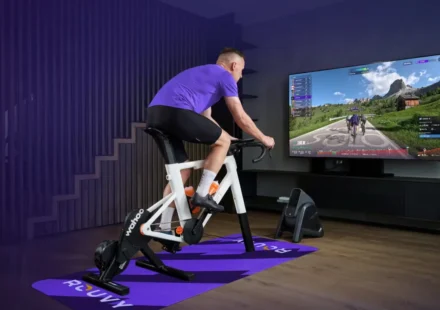 Man riding a smart indoor bike while Zwift displays a virtual cycling route on a large screen.
