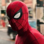 Spider Man in his iconic red suit stands on a city street, looking over his shoulder in daylight.