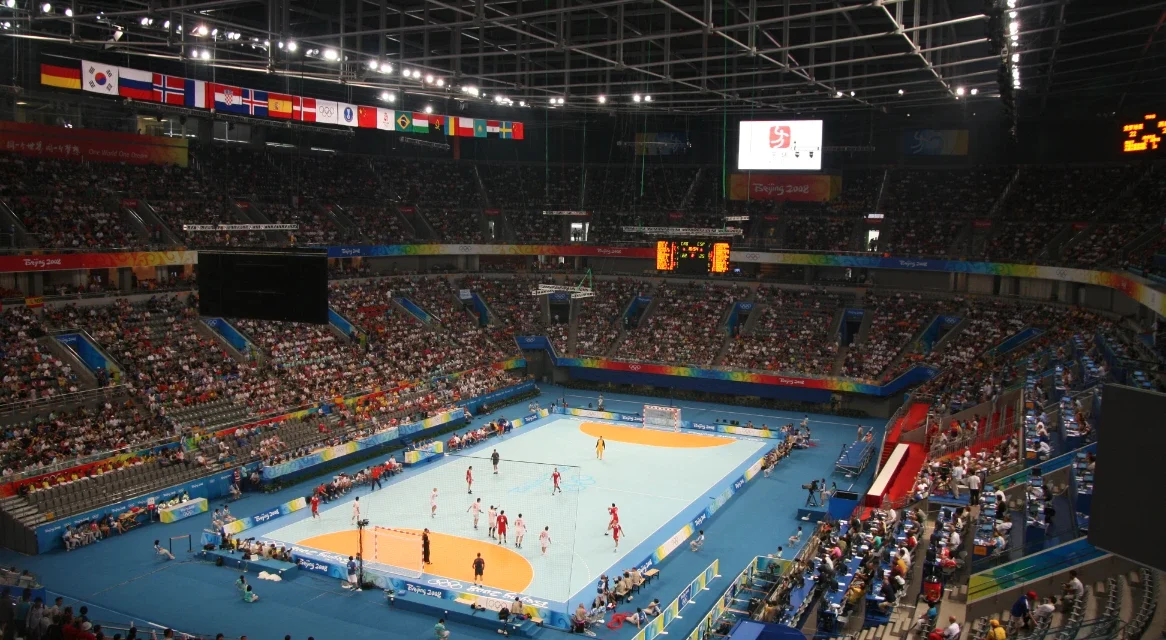 Crowded National Indoor Stadium hosts a handball match with athletes competing before a large crowd.
