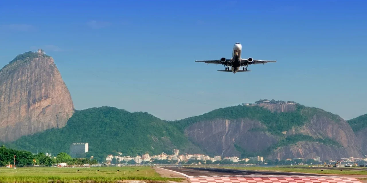Passenger plane approaches a runway with Rio de Janeiro's mountains and waterfront clearly in view.