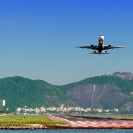 Passenger plane approaches a runway with Rio de Janeiro's mountains and waterfront clearly in view.